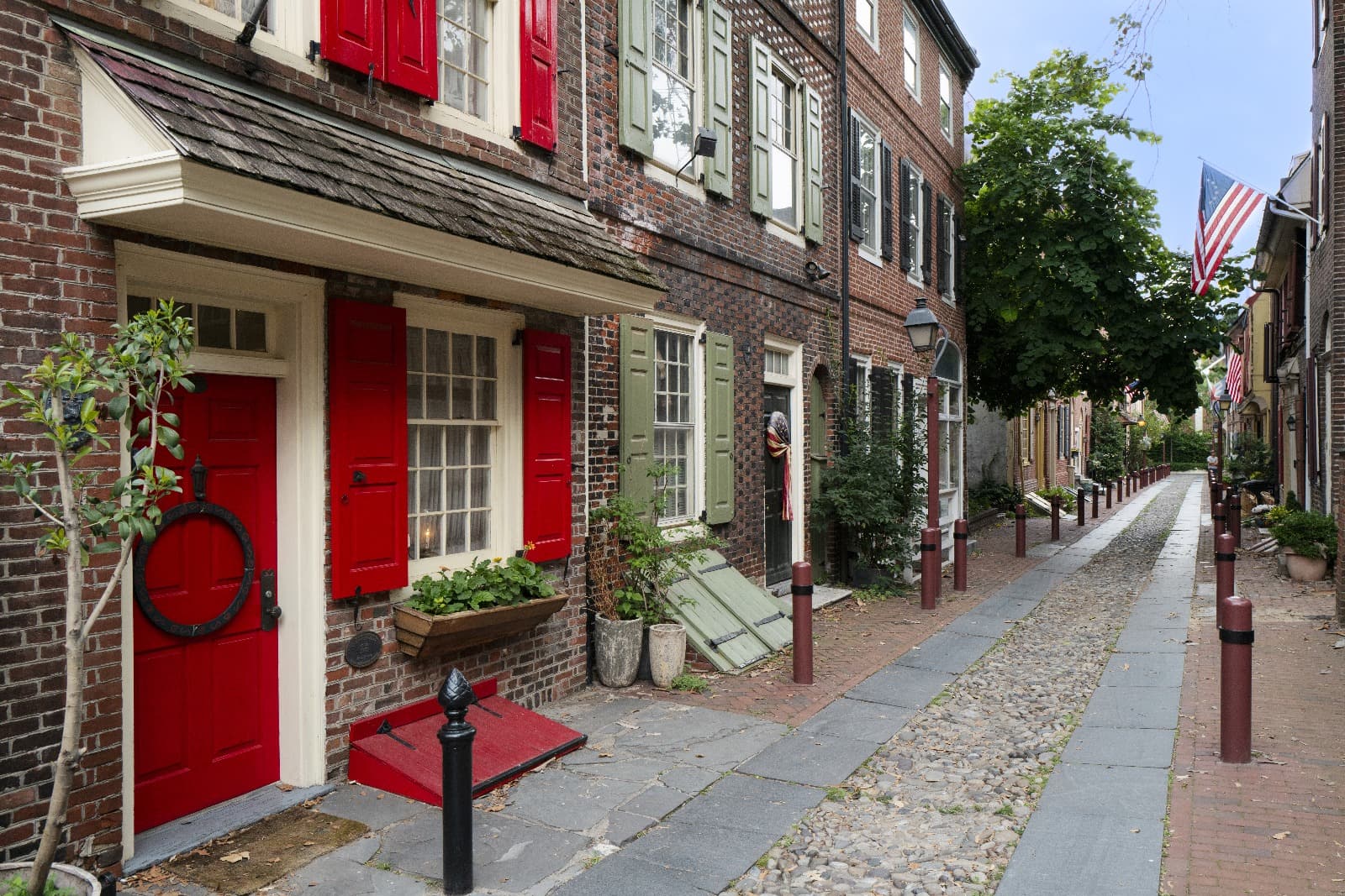 Historic brick row houses with red and green shutters and flower boxes along a narrow cobblestone street